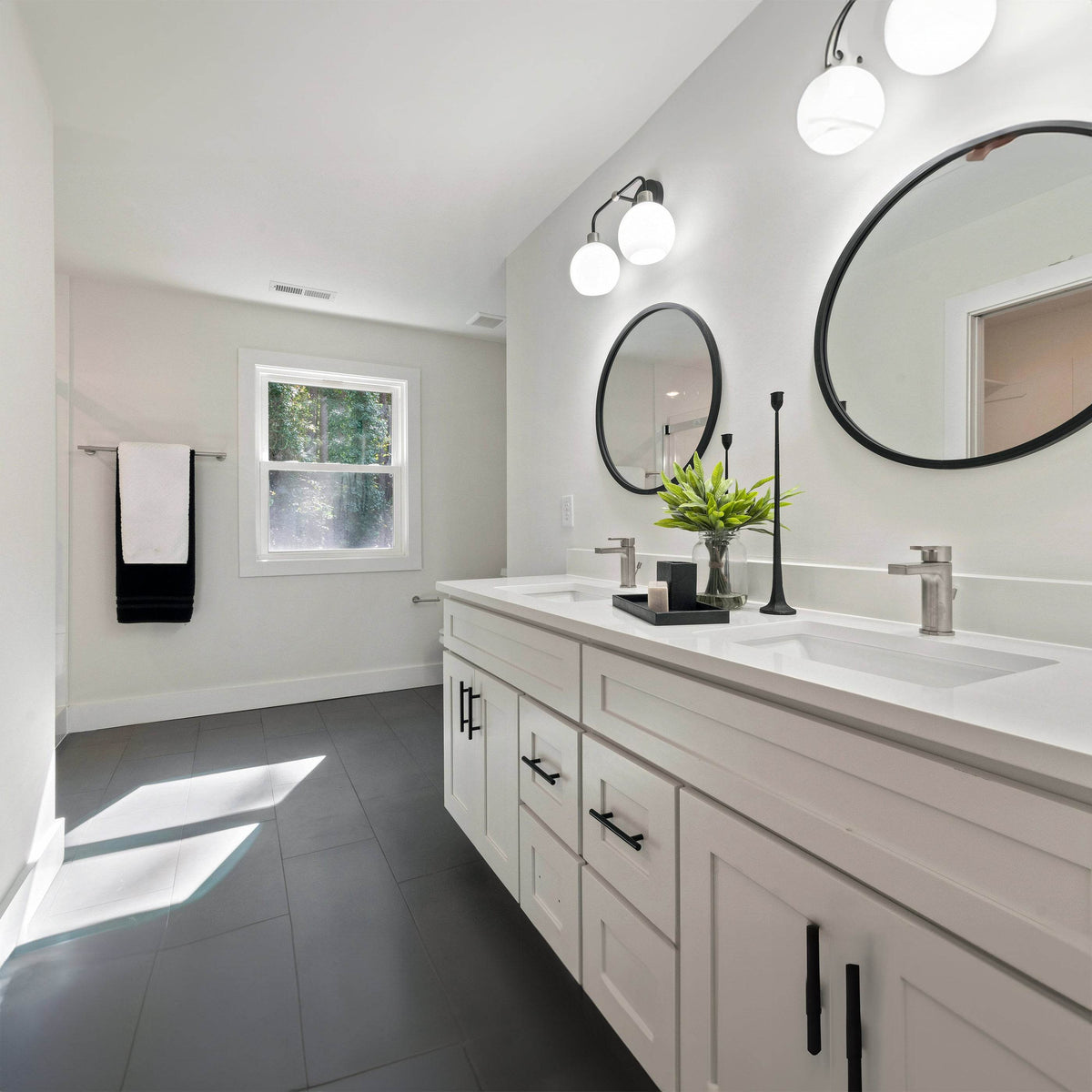 Modern white bathroom vanity with double sinks, black hardware, and round LED mirrors.