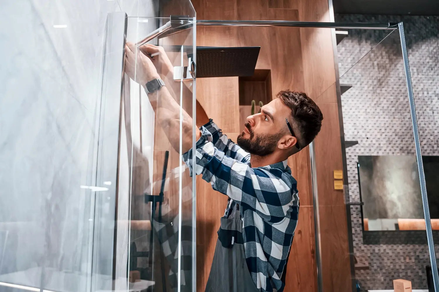 Technician installing a frameless glass shower enclosure, securing the top rail inside a modern tiled bathroom.