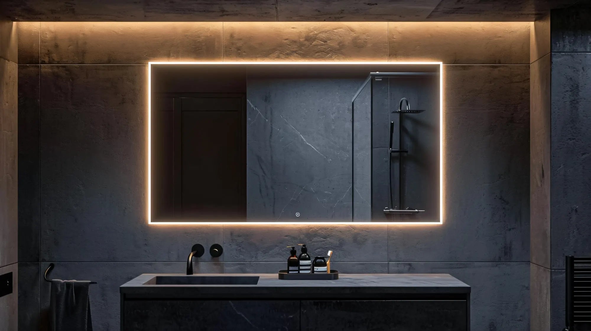 Large rectangular LED mirror with a warm light border and illuminated touch sensor buttons, mounted on a dark gray marble wall above a matching vanity with a black sink and faucet in a high-end, contemporary bathroom.