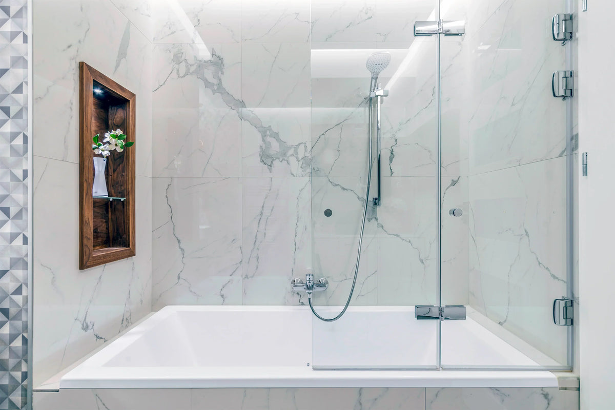Modern white bathtub with glass shower door and marble tile walls in a luxury bathroom.
