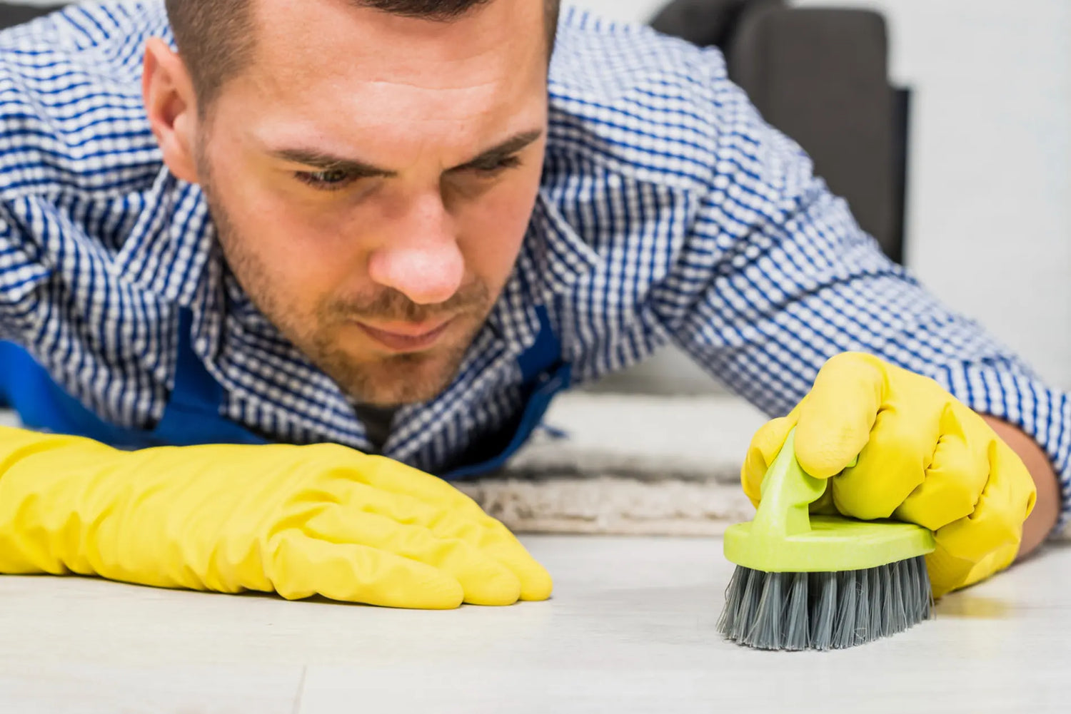 Man wearing yellow rubber gloves scrubs a shower base with a handheld cleaning brush.