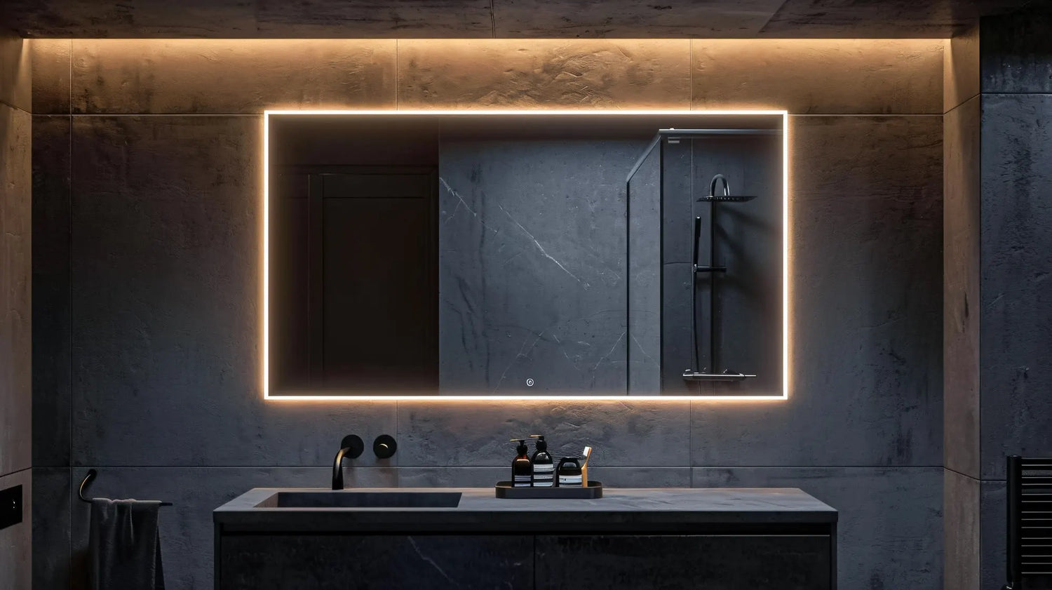Large rectangular LED mirror with a warm light border and illuminated touch sensor buttons, mounted on a dark gray marble wall above a matching vanity with a black sink and faucet in a high-end, contemporary bathroom.