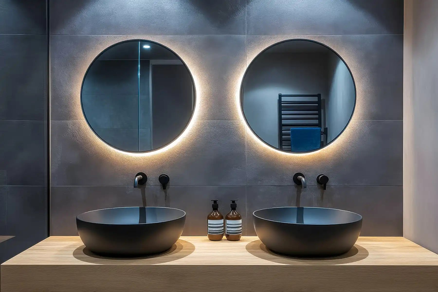 Modern bathroom with two round backlit mirrors and black vessel sinks on a vanity.