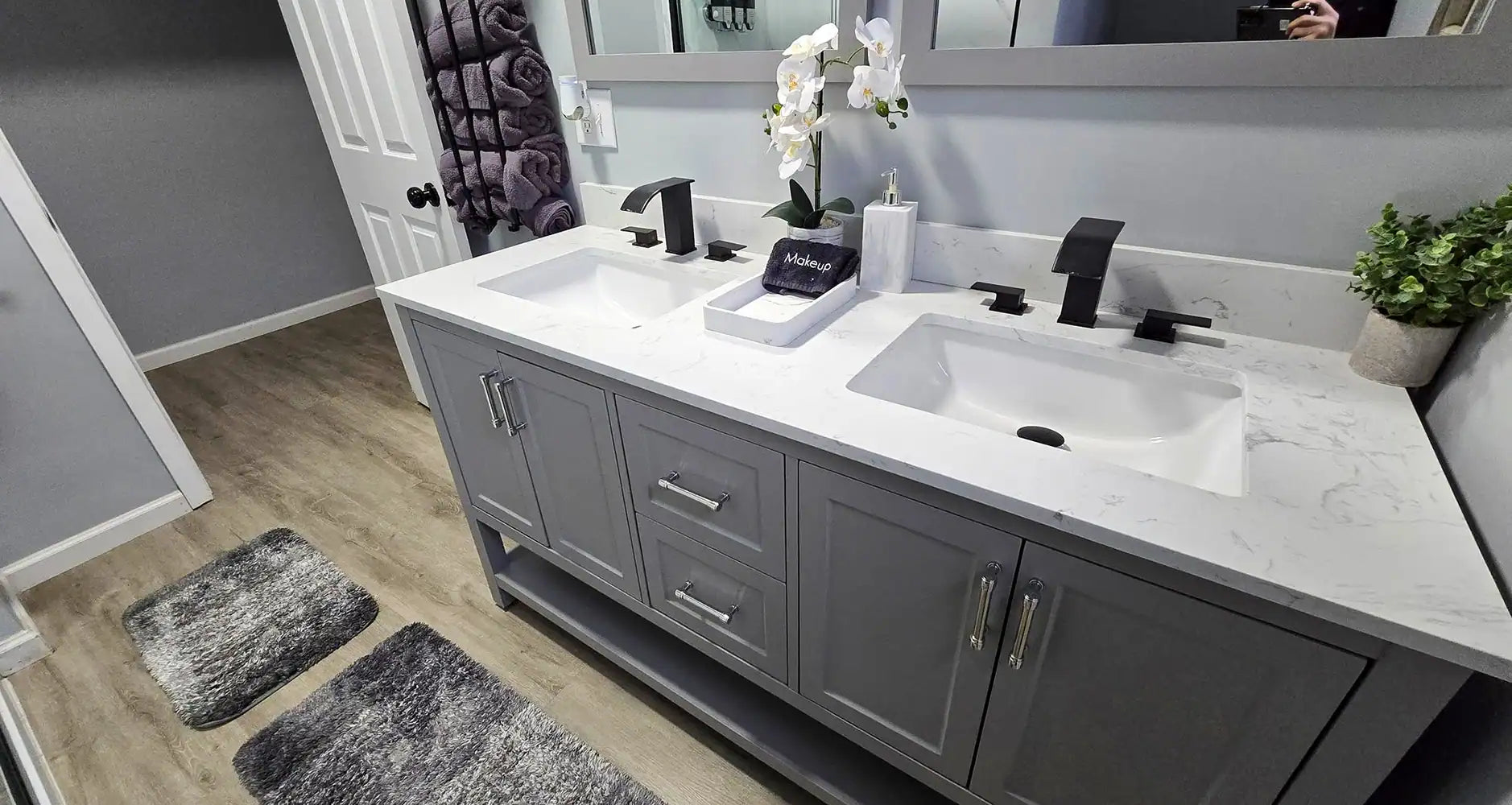 Gray double-sink bathroom vanity with a white marble-look countertop, black faucets, silver hardware, and a large wall mirror.