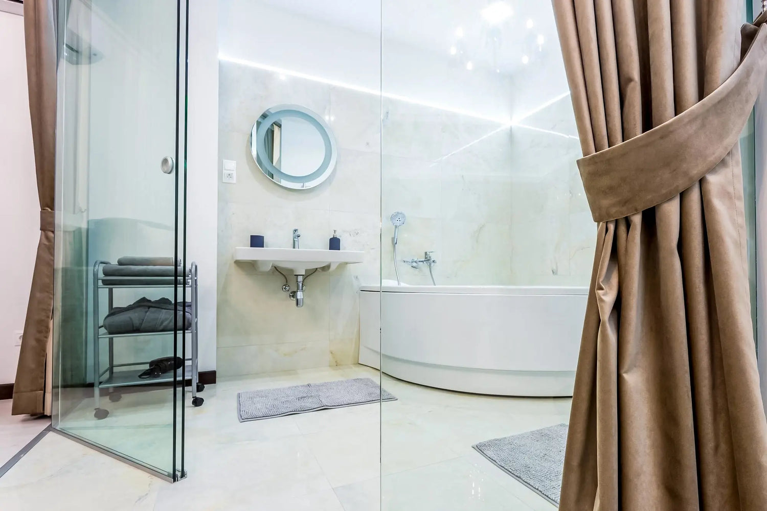 Minimal, spa-style bathroom with a glass shower screen, curved freestanding tub, wall-mounted sink, and taupe floor-length curtains.