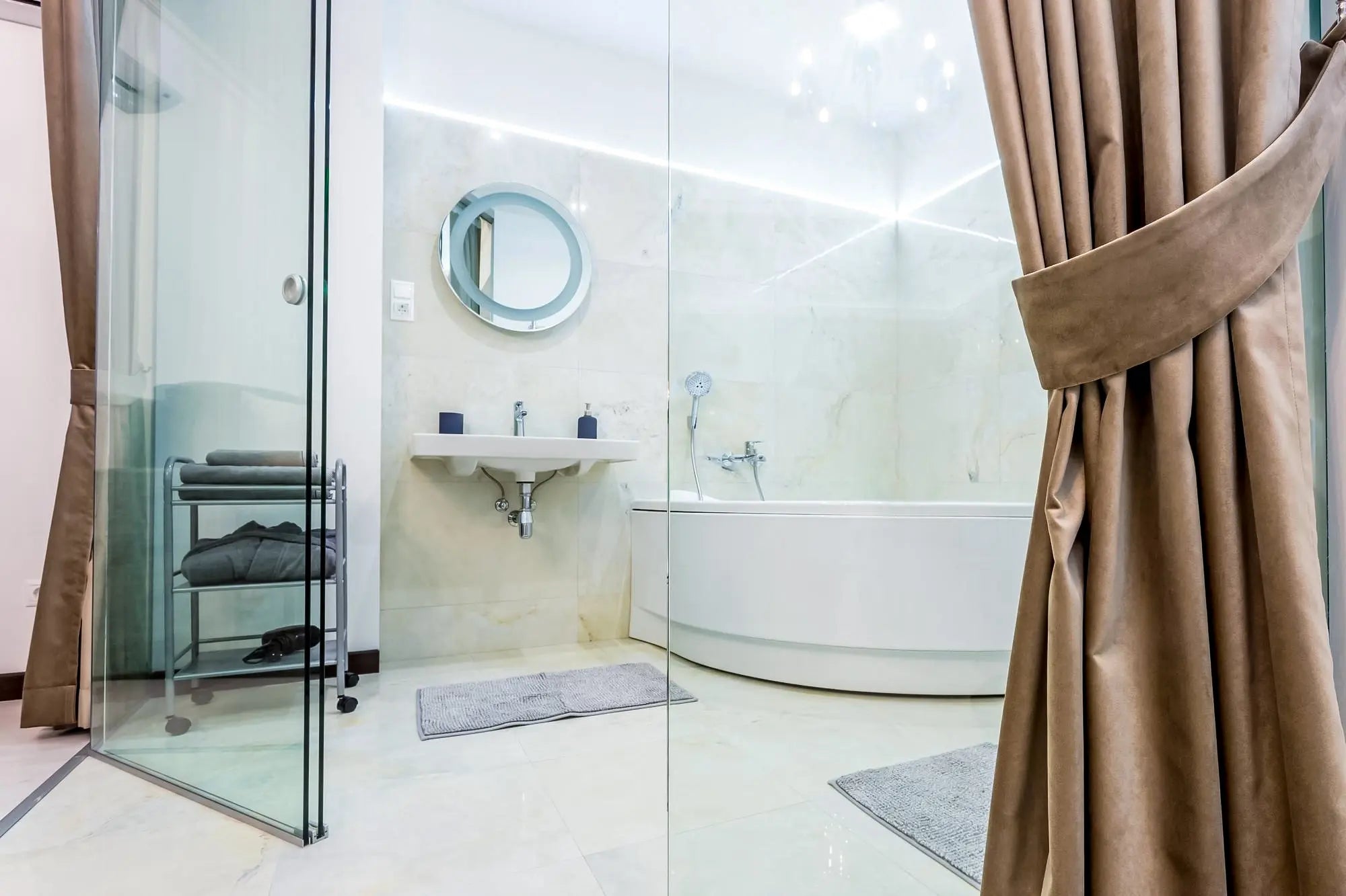 Minimal, spa-style bathroom with a glass shower screen, curved freestanding tub, wall-mounted sink, and taupe floor-length curtains.