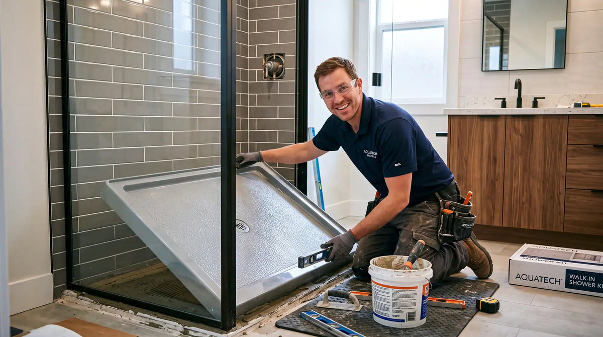 Installer positioning a shower base inside a black-framed glass enclosure while checking it with a level.