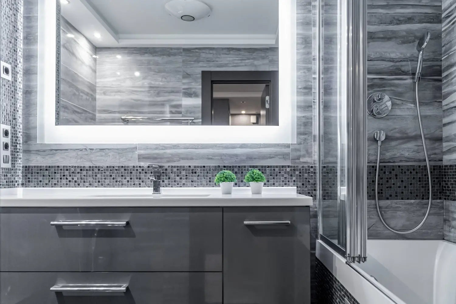 Big LED mirror in a luxury bathroom lighted up with bathtub on the side and floating white vanity.