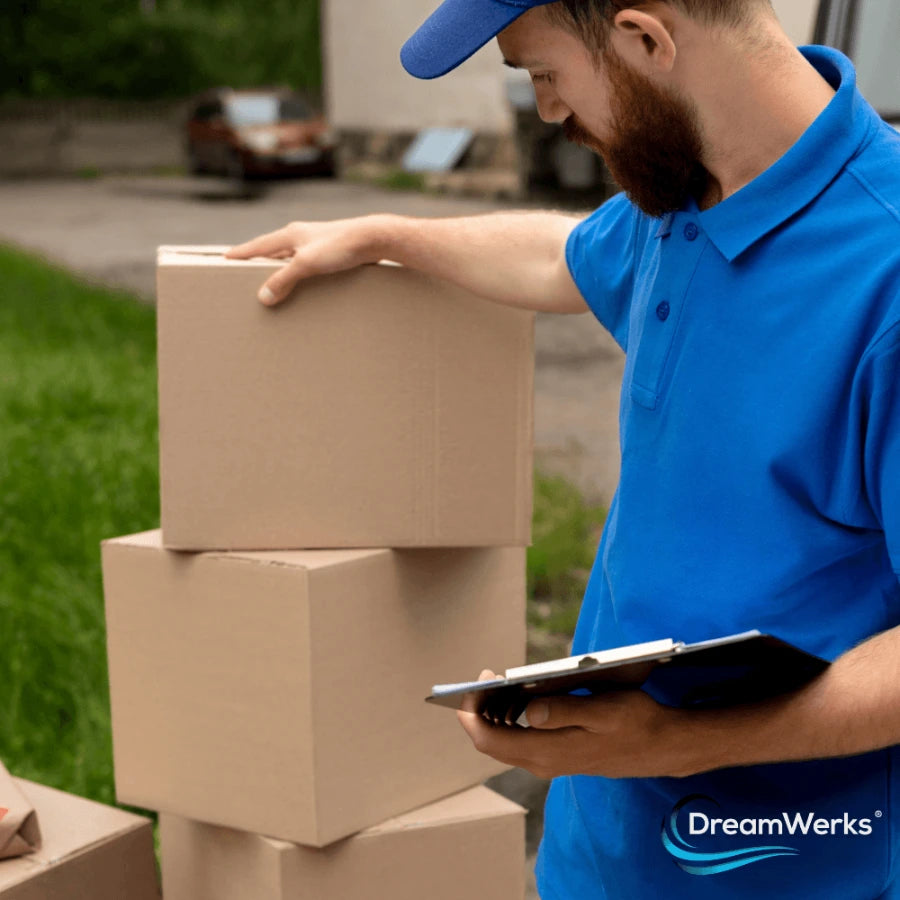 Man in blue shirt with Dreamwerks logo holding a stack of cardboard boxes and a tablet for delivery.