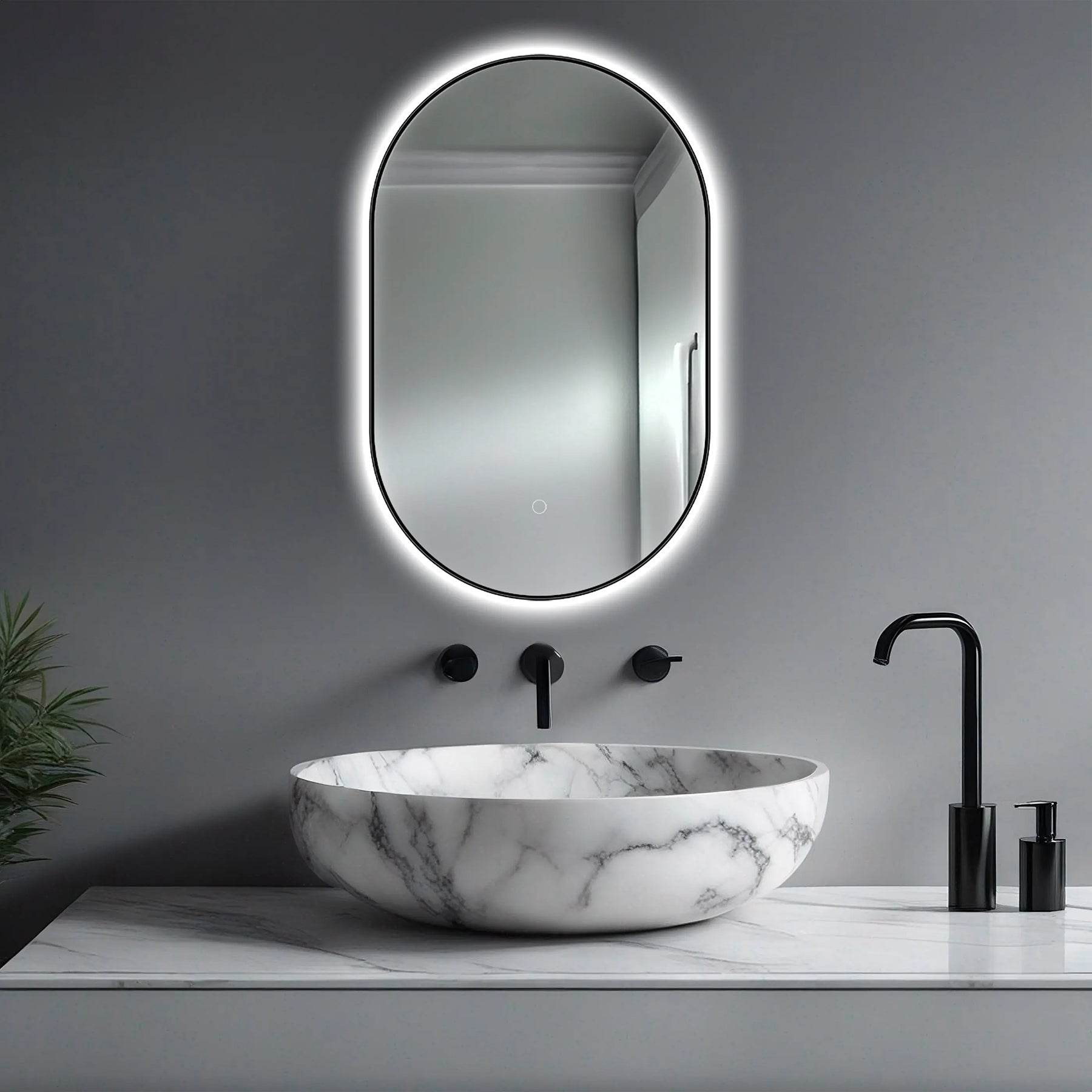 An LED lighted bathroom mirror with a dimmer and defogger in a modern black frame, mounted above a white marble sink in a bathroom setting.