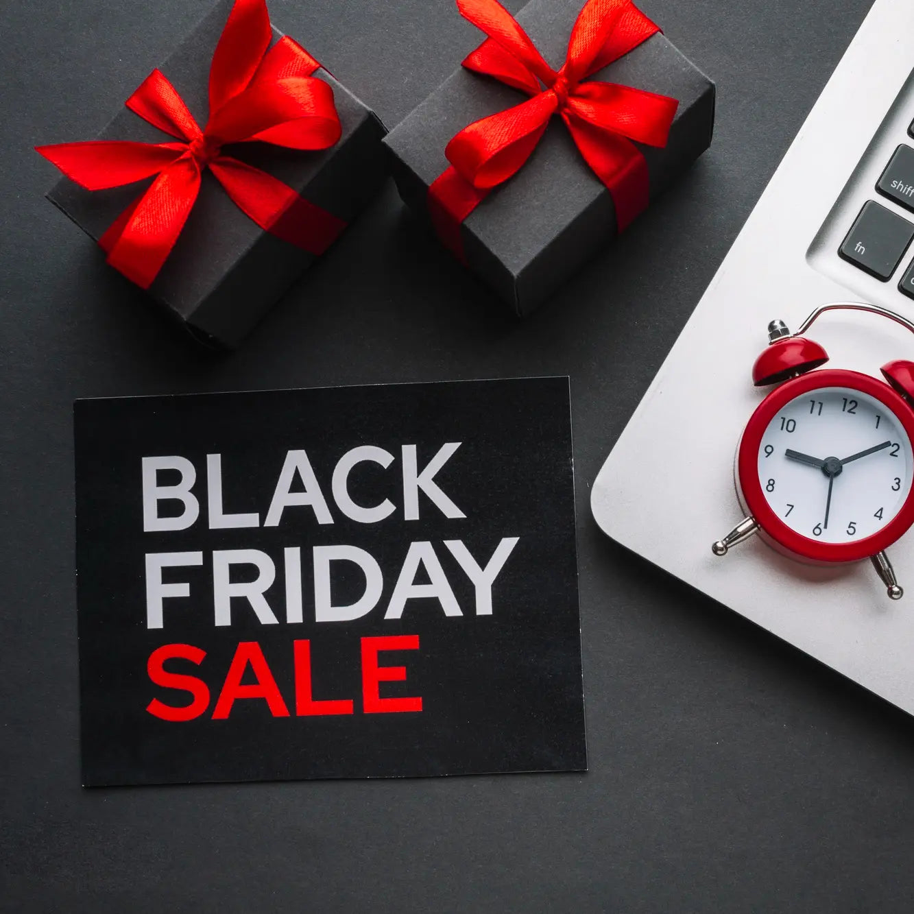 Black Friday sale sign with gift boxes, red alarm clock, and laptop on a dark surface