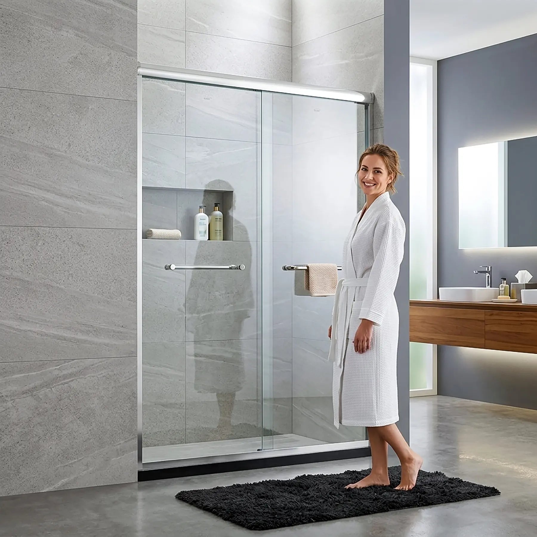 Woman in a white robe standing in a modern bathroom with a glass shower enclosure.
