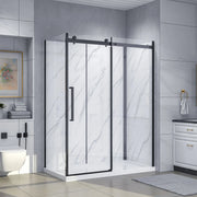 Dreamwerks Bristol 60-inch corner shower kit with sliding door, matte black frame, clear tempered glass panels, white marble-look shower walls, and a matching white base. The unit is installed in a modern bathroom with gray tiled walls.