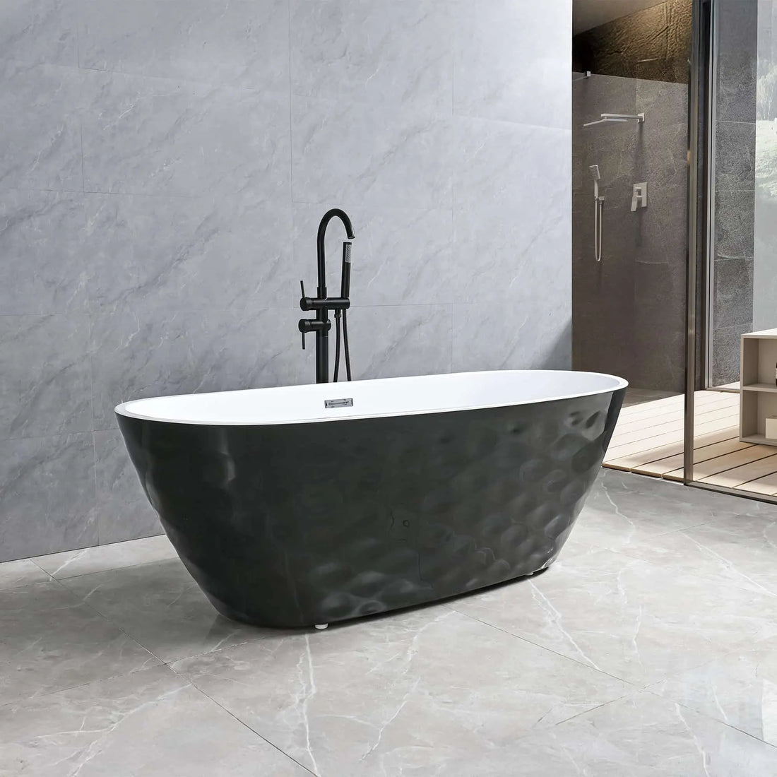 Dreamwerks Corvino Contemporary bathroom featuring a freestanding oval bathtub with a black, textured, wavy exterior skirt and a white interior. The tub is paired with a matte black floor-mounted faucet and is set against large format gray marble-look tile walls and floor. A walk-in glass shower enclosure is visible in the background.