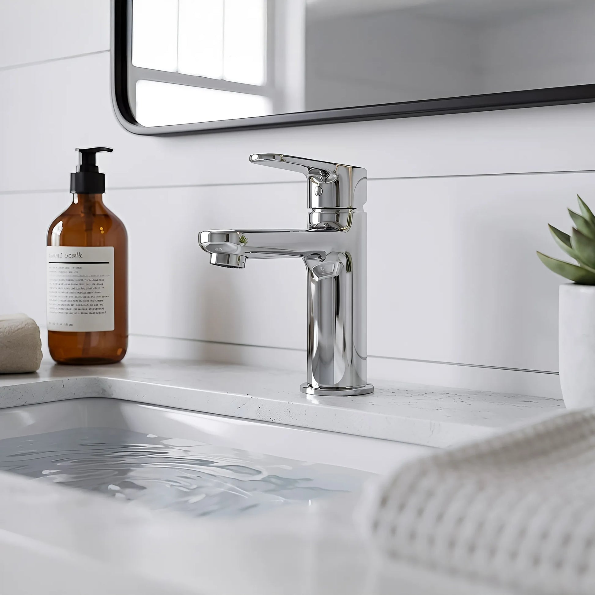 Modern kitchen sink with faucet, bottle, and plant on a white countertop.
