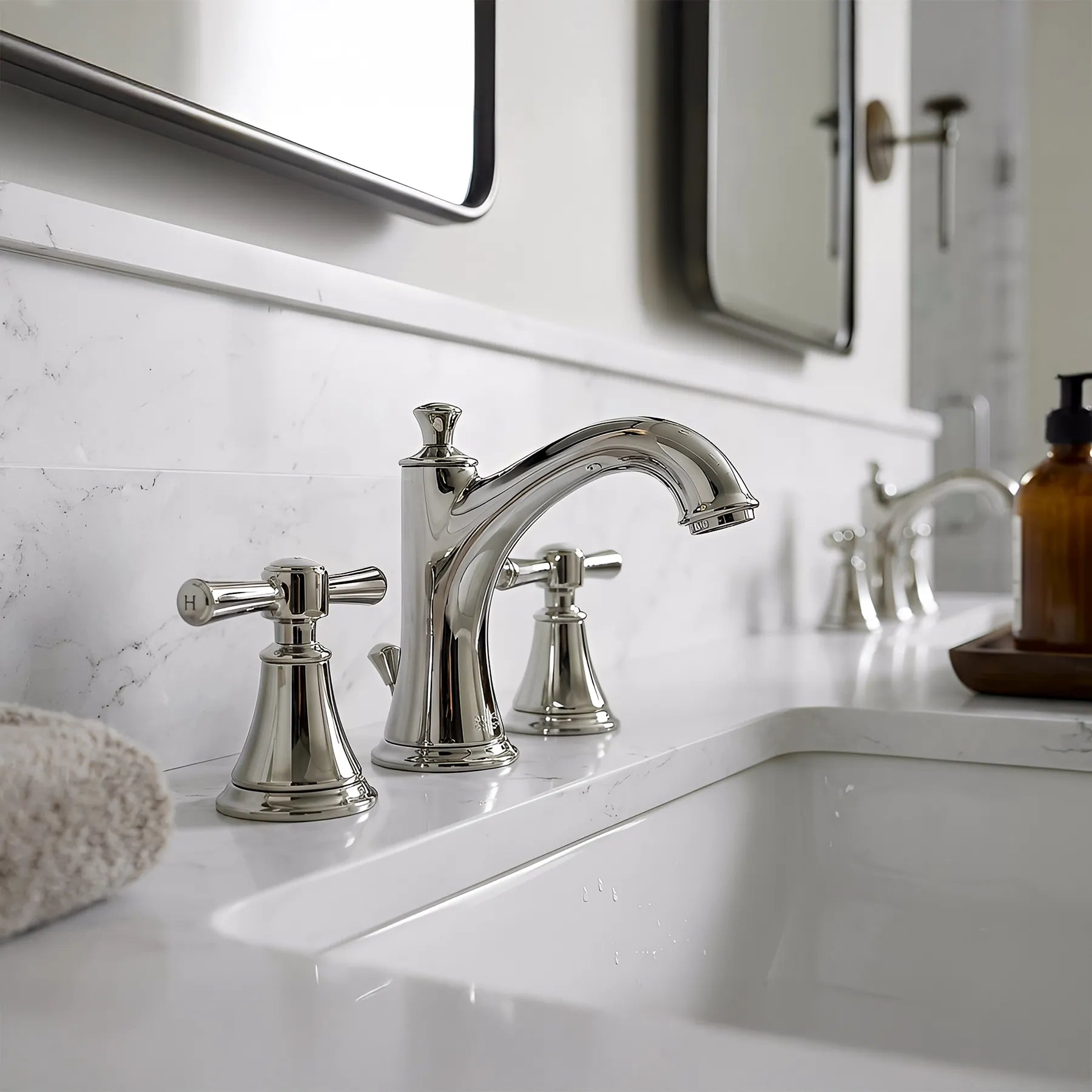 Chrome faucet on a bathroom sink with marble wall and mirror in the background