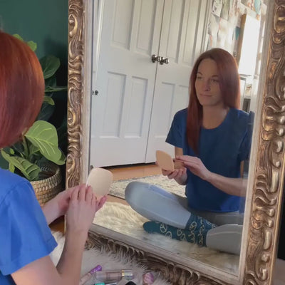 Video showing a woman using the Allegra LED mirror in her vanity area for her morning routine. It demonstrates the features, including the mirror's bright adjustable lighting for makeup application, the ability to open the mirror for hidden storage, and the integrated Bluetooth speaker and wireless phone charging shelf.