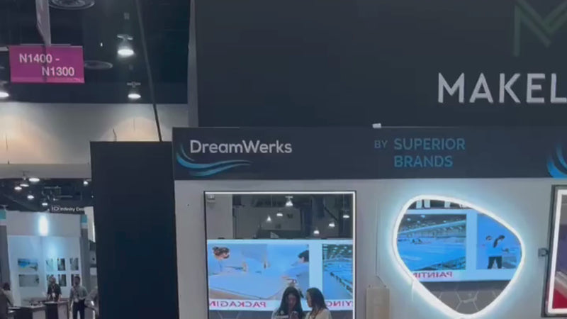 Video showing the DreamWerks booth at the KBIS 2024 trade show, displaying a variety of modern bathroom products. The video highlights smart LED mirrors in different shapes (rectangular, oval, and organic) with integrated video screens and touch controls, as well as several white freestanding bathtubs and a close-up of a shower door handle. It ends with the DreamWerks logo.